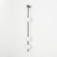 Wall lamp with a vertical row of white ball shades on a slim dark rod, unlit, on a white background.