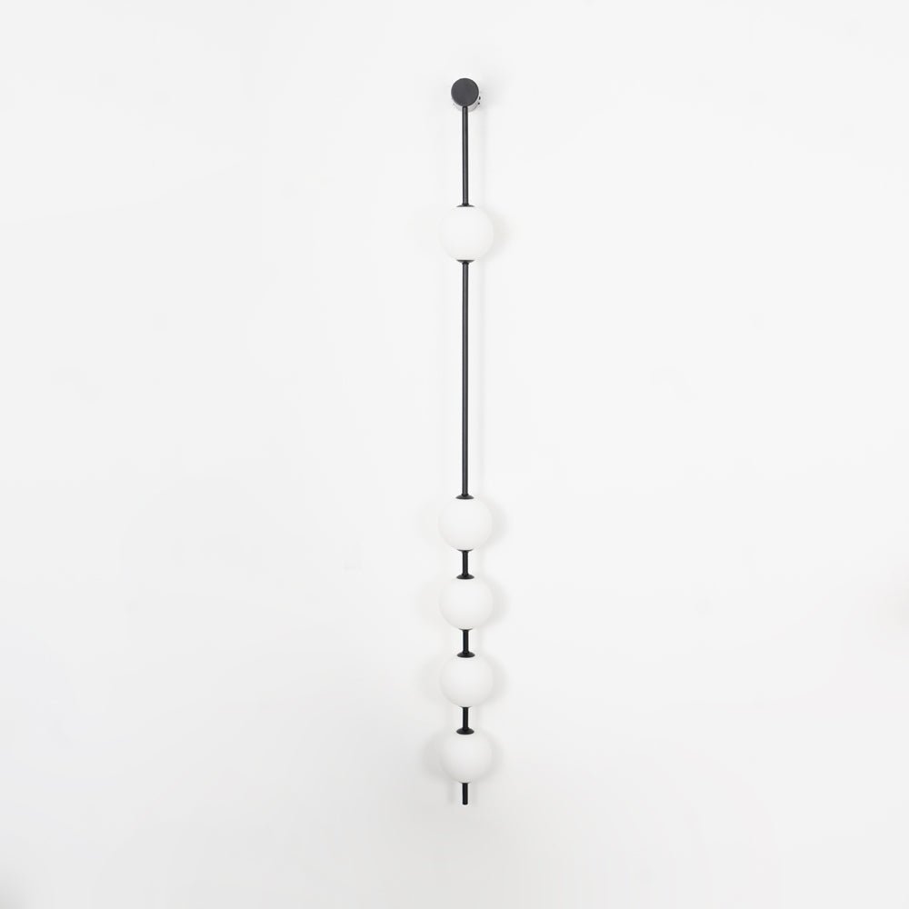 Wall lamp with a vertical row of white ball shades on a slim dark rod, unlit, on a white background, seen straight on.