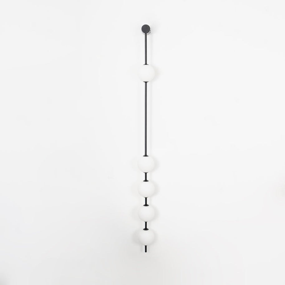 Wall lamp with a vertical row of white ball shades on a slim dark rod, unlit, on a white background, seen straight on.