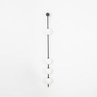 Wall lamp with a vertical row of white ball shades on a slim dark rod, unlit, on a white background.