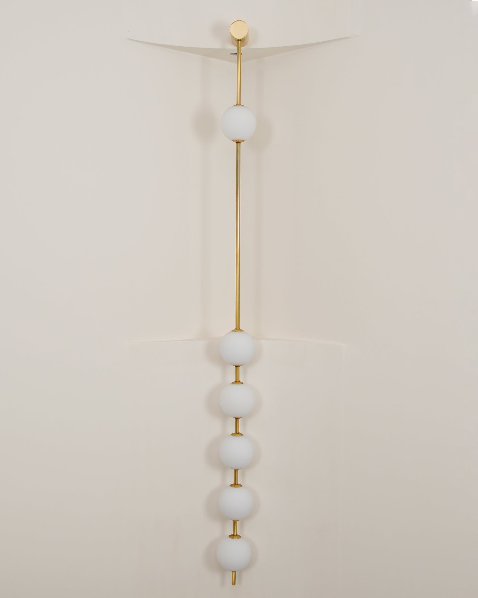 Wall lamp with a vertical row of white ball shades on a slim rod, unlit, against a pale wall.