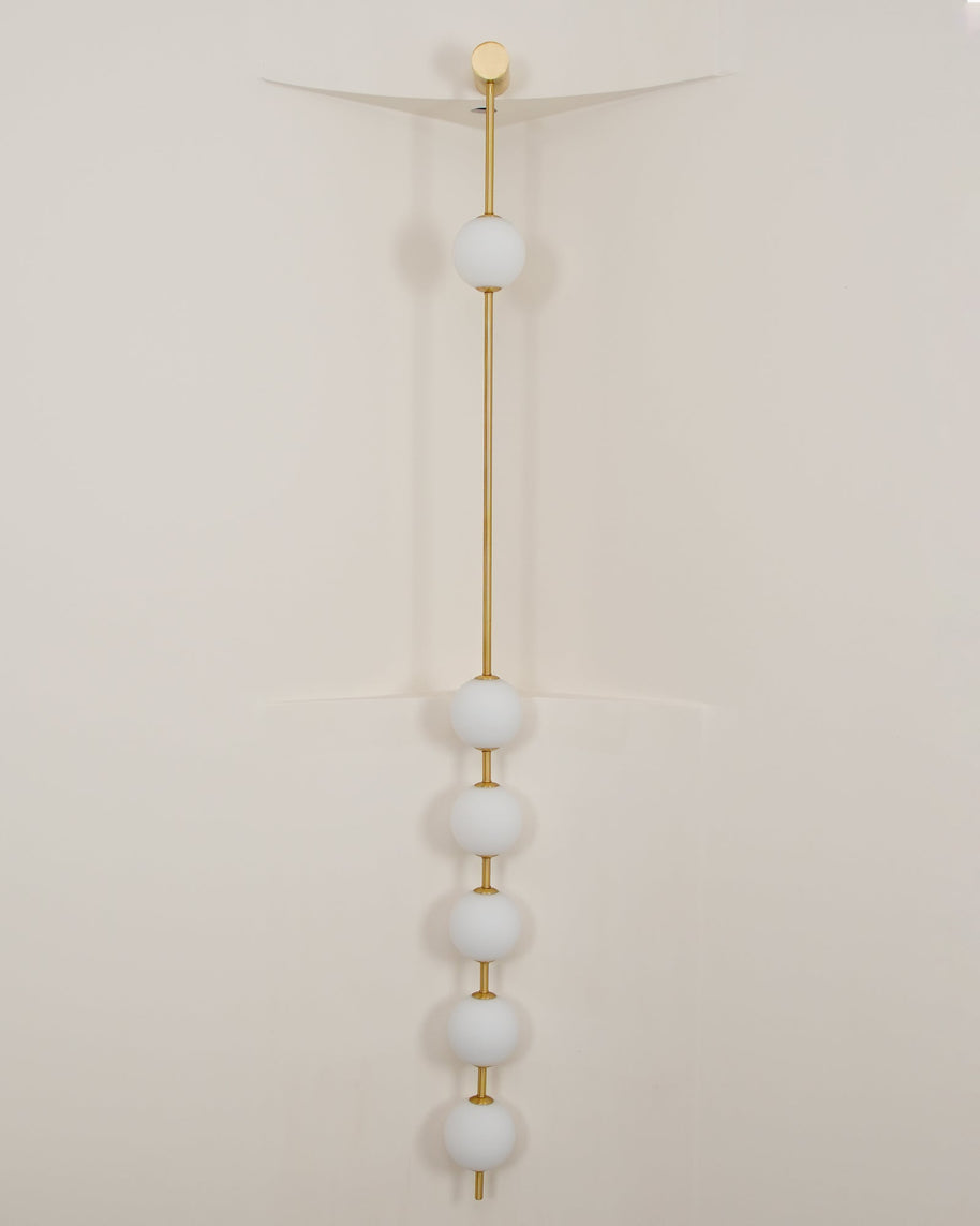 Wall lamp with a vertical row of white ball shades on a slim rod, unlit, against a pale wall.