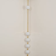 Wall lamp with a vertical row of white ball shades on a slim rod, unlit, against a pale wall.