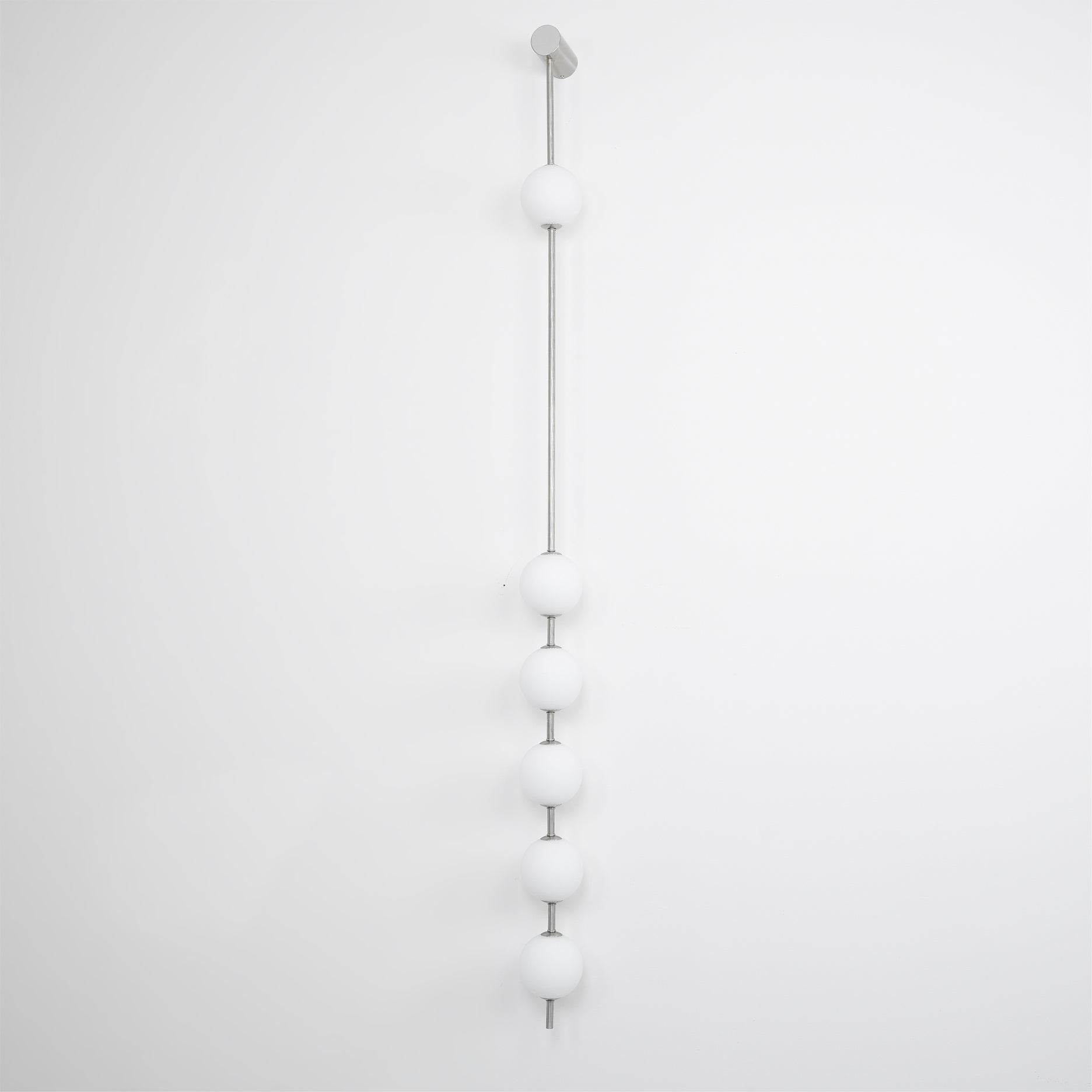 Wall lamp with a vertical row of white ball shades on a slim nickel-coloured rod, unlit, on a white wall.