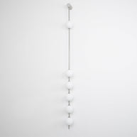 Wall lamp with a vertical row of white ball shades on a slim nickel-coloured rod, unlit, on a white wall.