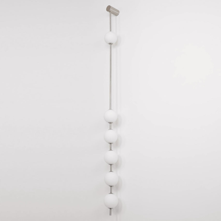 Wall lamp with a vertical row of white ball shades on a slim nickel-coloured rod, unlit, on a white wall.