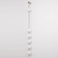 Wall lamp with a vertical row of white ball shades on a slim nickel-coloured rod, unlit, on a white wall.