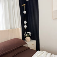 Wall lamp with a vertical row of white ball shades on a slim brass-coloured rod lit in a bedroom corner with navy panelling.