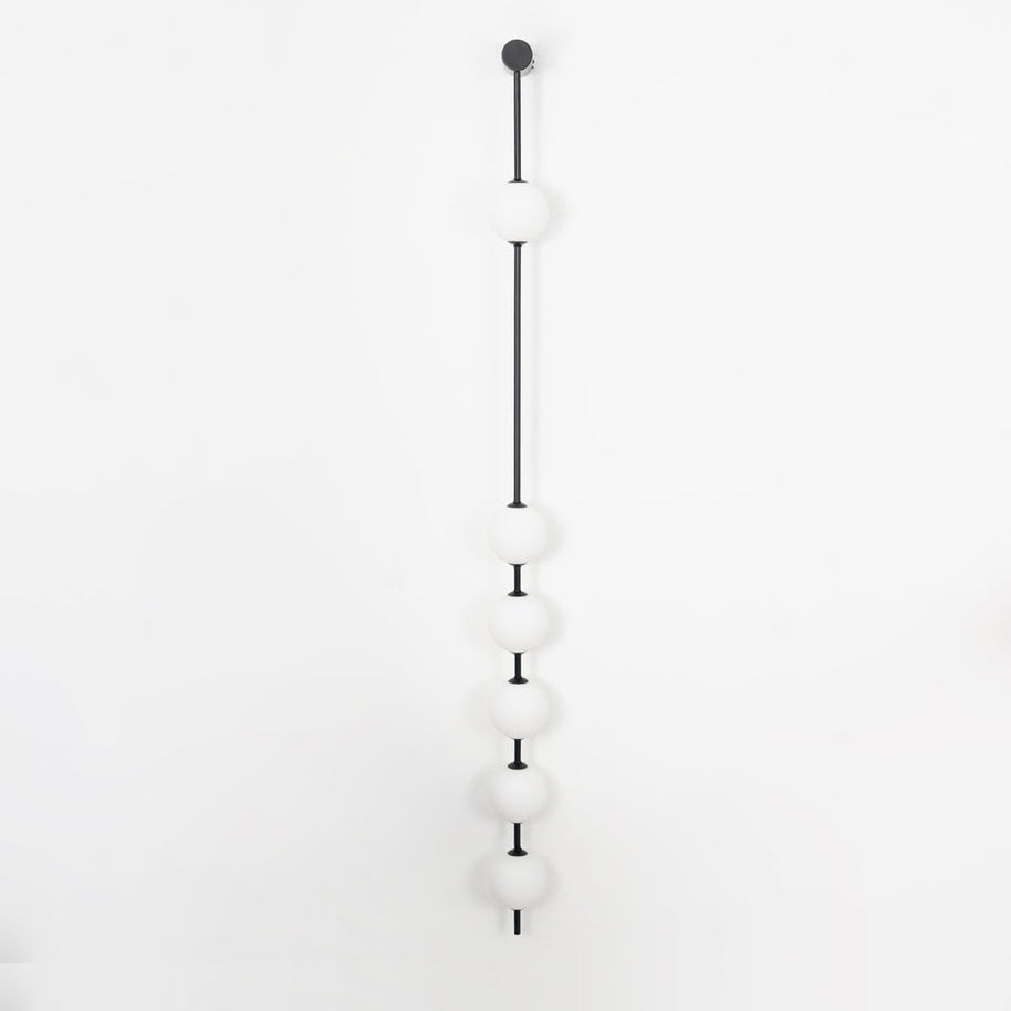 Wall lamp with a vertical row of white ball shades on a slim dark rod, unlit, on a pale background.