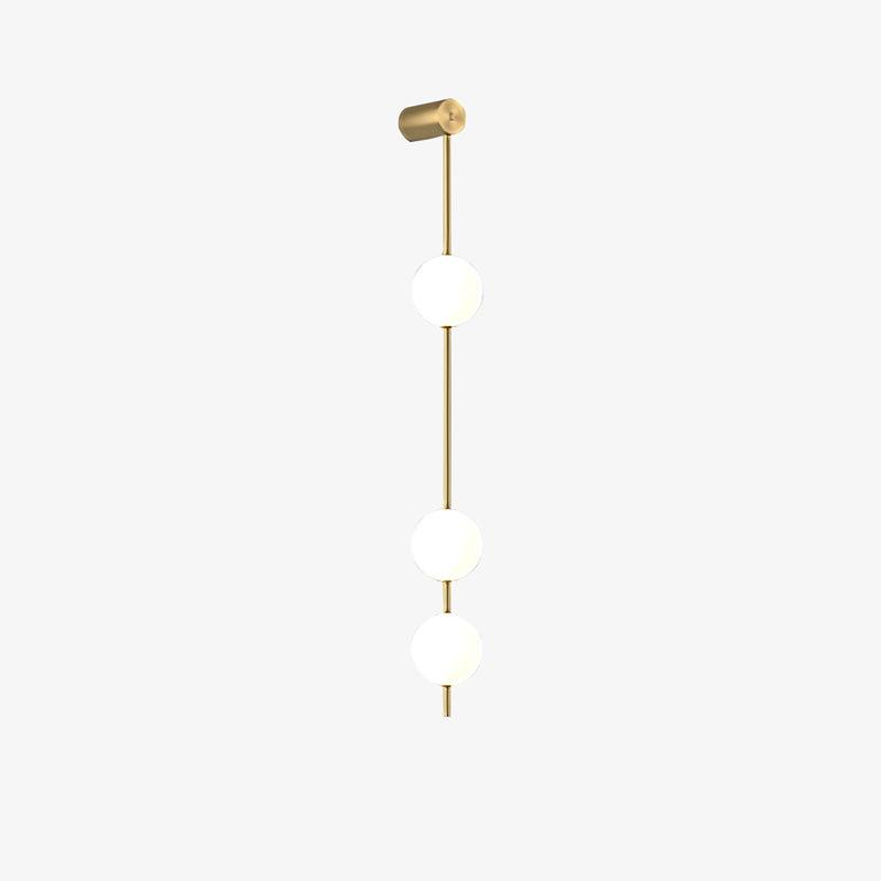 Wall lamp with a vertical row of white ball shades on a slim brass-coloured rod, unlit, on a white background, with a short row of shades.