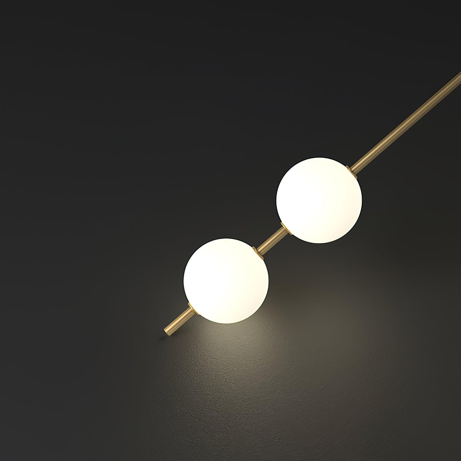 Close view of a slim gold-toned rod carrying white ball shades, lit, against a dark background.