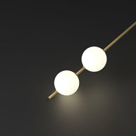 Close view of a slim gold-toned rod carrying white ball shades, lit, against a dark background.
