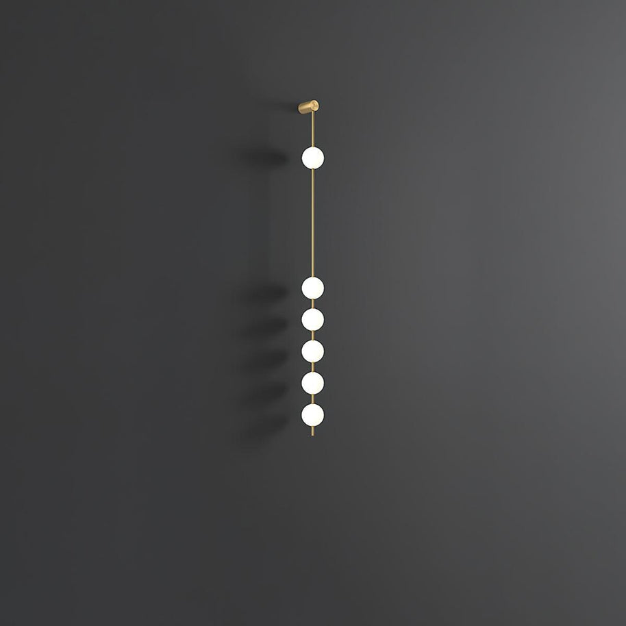 Wall lamp with a vertical row of white ball shades on a slim brass-coloured rod, unlit, on a grey wall.