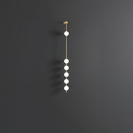 Wall lamp with a vertical row of white ball shades on a slim brass-coloured rod, unlit, on a grey wall.