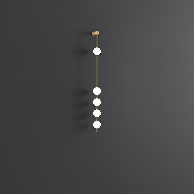 Wall lamp with a vertical row of white ball shades on a slim brass-coloured rod, unlit, on a grey wall.