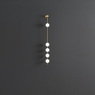 Wall lamp with a vertical row of white ball shades on a slim brass-coloured rod, unlit, on a grey wall.