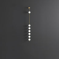 Wall lamp with a vertical row of white ball shades on a slim brass-coloured rod, unlit, on a grey wall.
