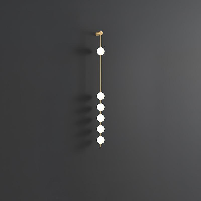 Wall lamp with a vertical row of white ball shades on a slim brass-coloured rod, unlit, on a grey wall.