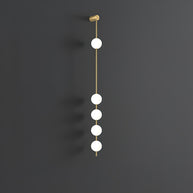 Wall lamp with a vertical row of white ball shades on a slim brass-coloured rod, unlit, on a grey wall.