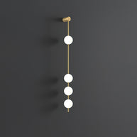 Wall lamp with a vertical row of white ball shades on a slim brass-coloured rod, unlit, on a grey wall.