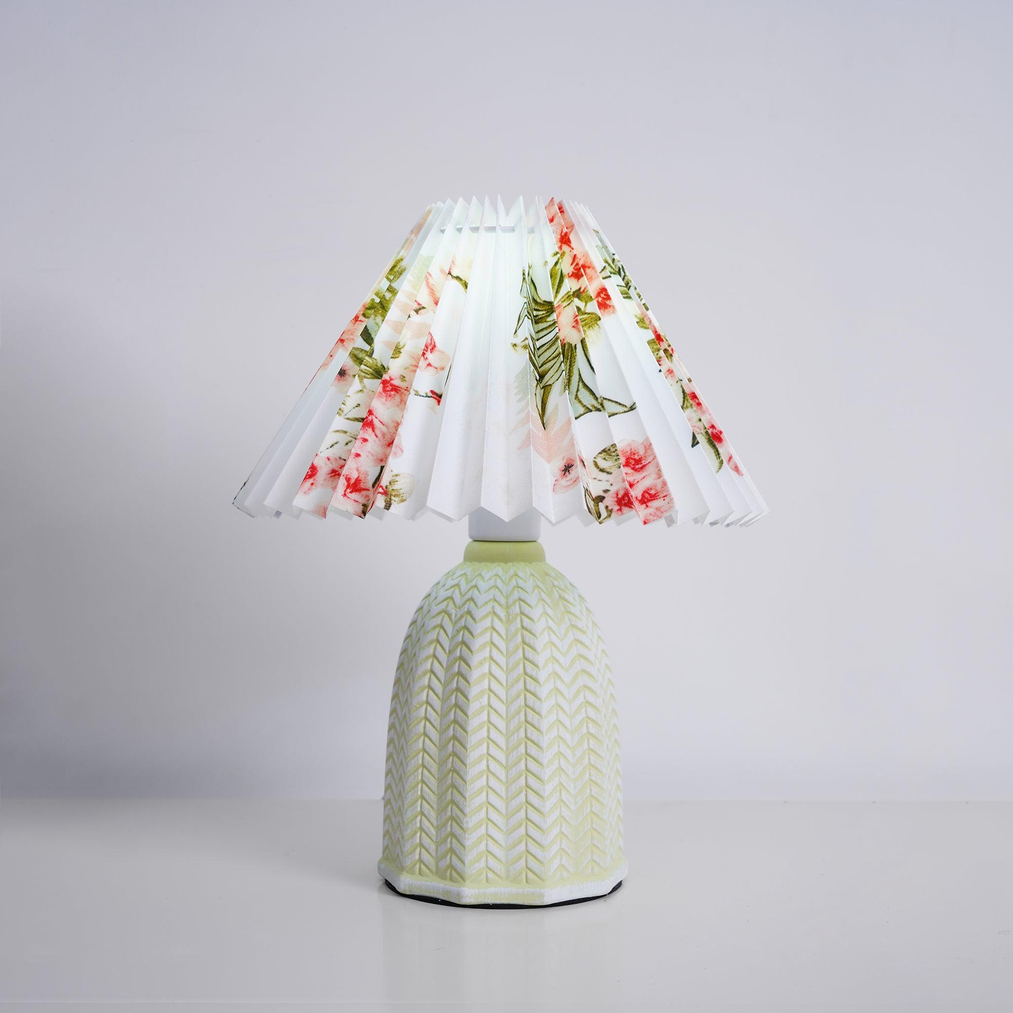 Table lamp with a white pleated shade in a printed floral pattern and a pale green ceramic base with a raised chevron pattern, shown on a pale grey background.