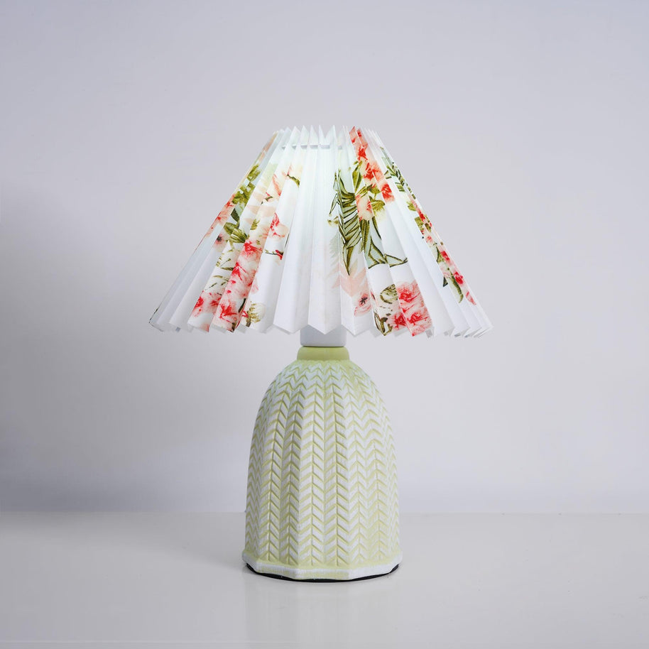 Table lamp with a white pleated shade in a printed floral pattern and a pale green ceramic base with a raised chevron pattern, shown on a pale grey background.