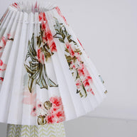 Table lamp with a white pleated shade in a printed floral pattern and a pale green ceramic base with a raised chevron pattern, seen close from below on a plain background.