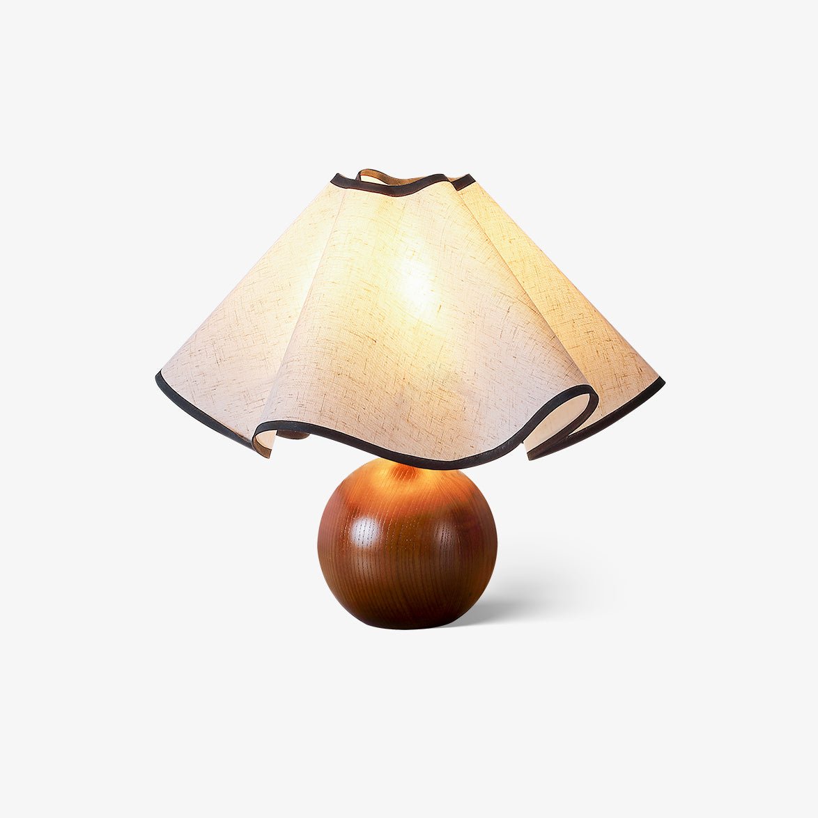 Table lamp with a wavy black-trimmed linen shade on a walnut sphere base, lit, on a plain white background.