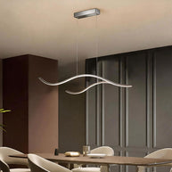 Linear pendant light made of wavy chrome-coloured LED bars hung from a slim rectangular canopy above a dining table beside dark panelling.