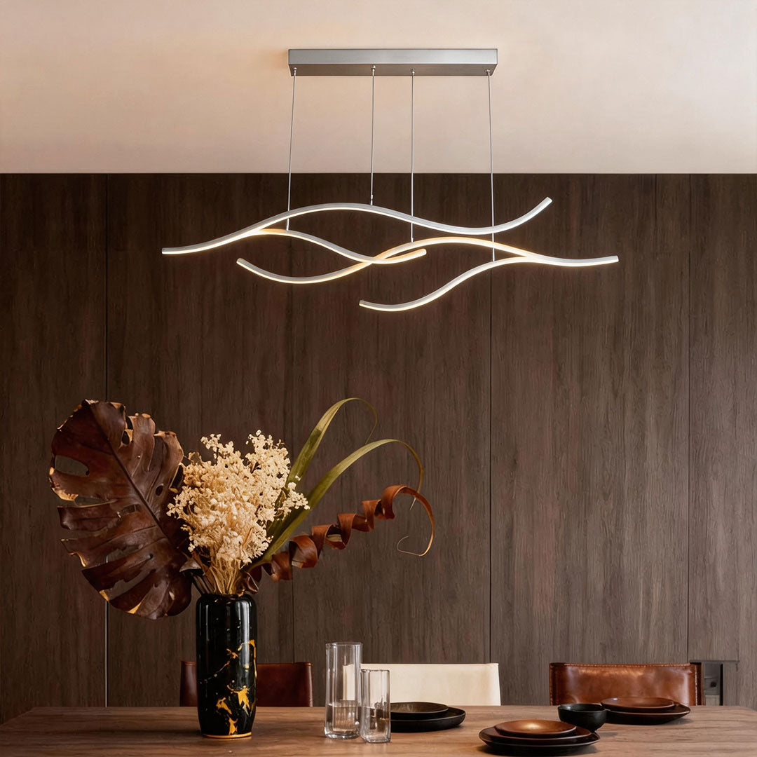 Linear pendant light made of wavy chrome-coloured LED bars hung from a slim rectangular canopy above a table against a walnut-panelled wall.