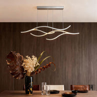 Linear pendant light made of wavy chrome-coloured LED bars hung from a slim rectangular canopy above a table against a walnut-panelled wall.