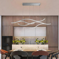 Linear pendant light made of wavy chrome-coloured LED bars hung from a slim rectangular canopy above a dining table in a wood-panelled room.