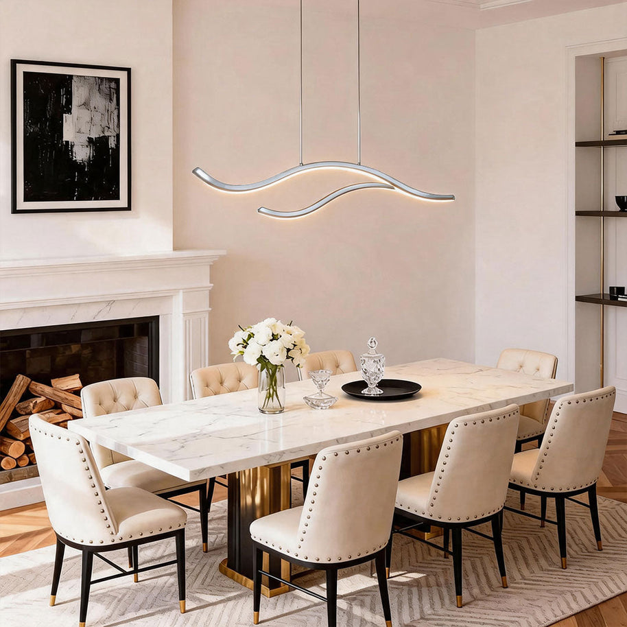 Linear pendant light made of wavy chrome-coloured LED bars hung from a slim rectangular canopy above a marble dining table beside a fireplace.