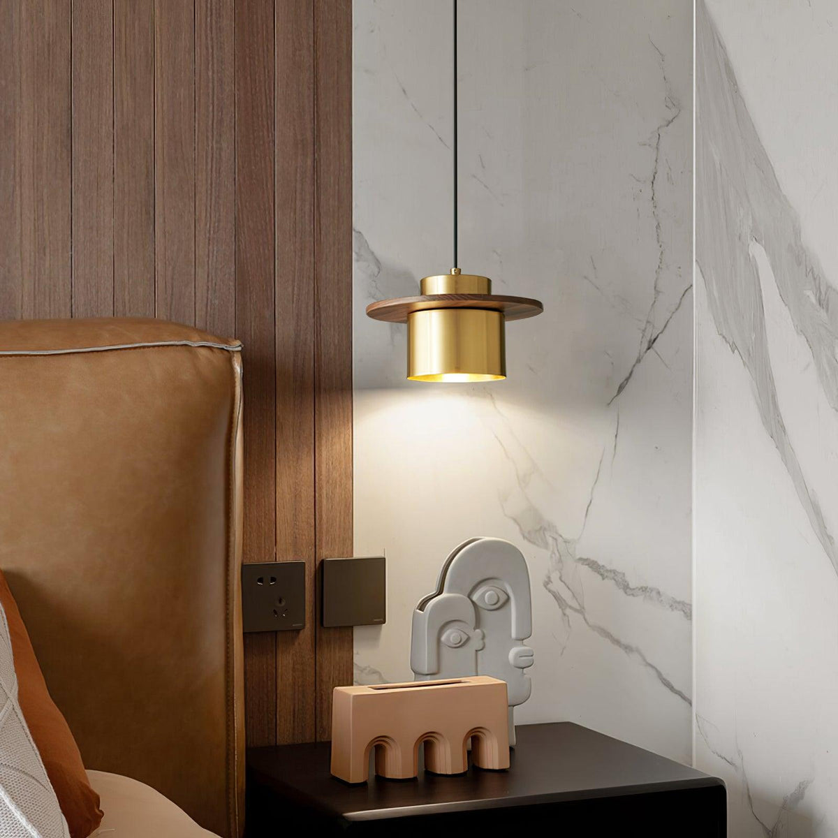 Belsora Pendant Light in brass and walnut lit above a bedside table by a marble wall