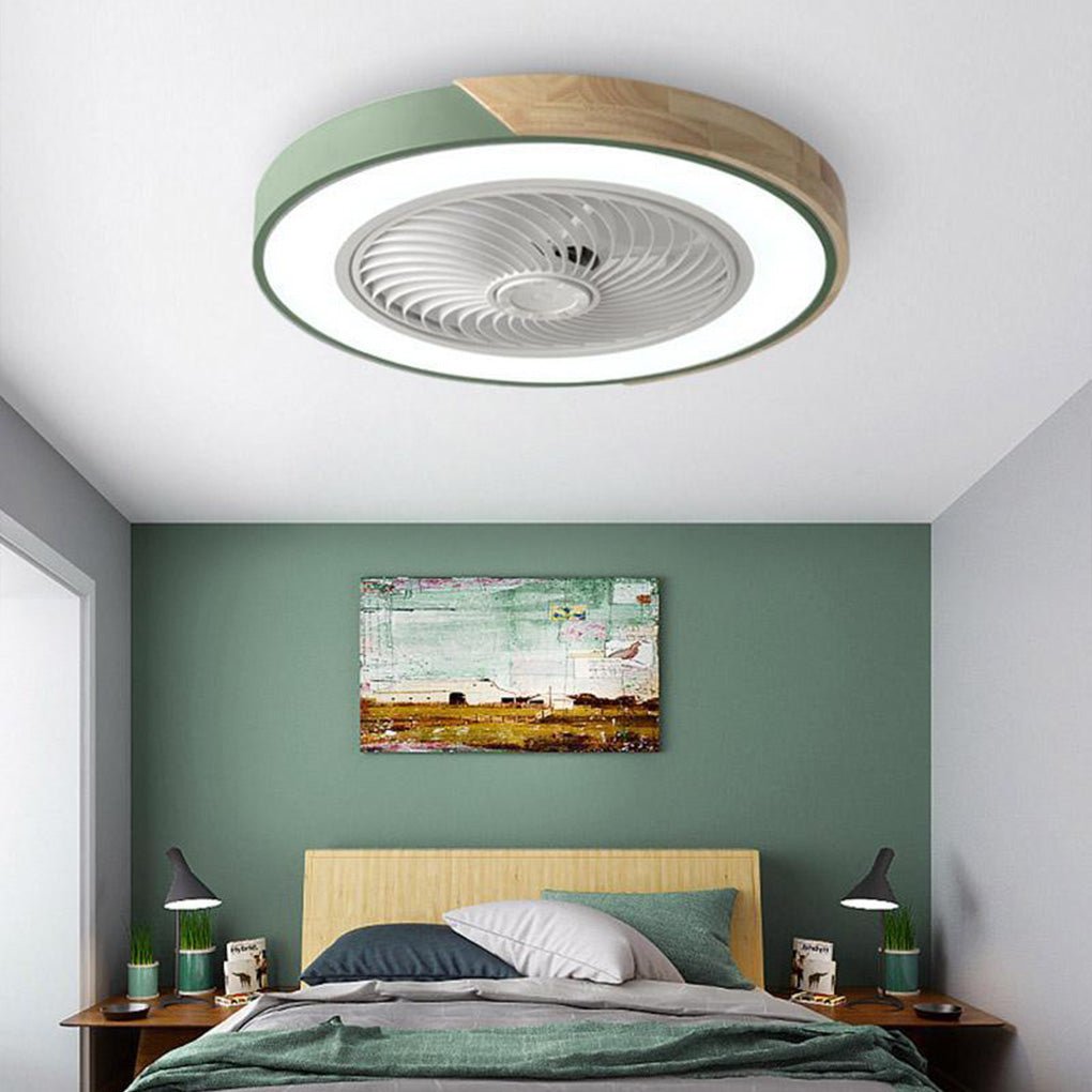 Round green and wood-grain bladeless ceiling fan with light, lit, on a bedroom ceiling, with a bed and a green wall below.