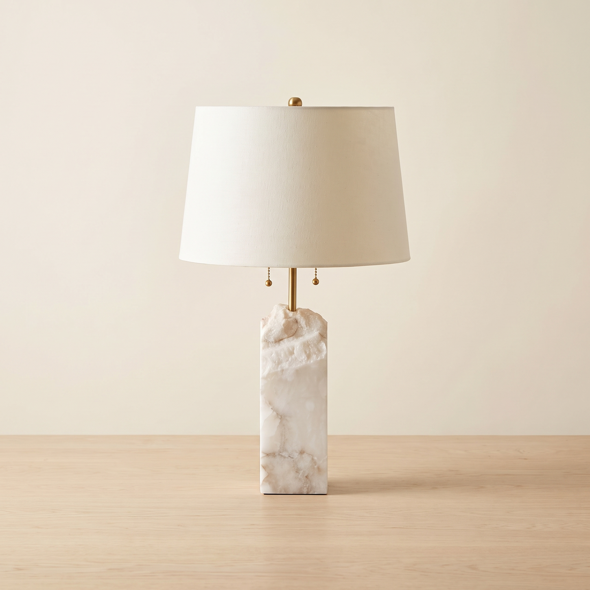Pallidine Raw Alabaster Table Lamp: table lamp with a rectangular raw white alabaster block base with natural veining, a slim brass stem, a cream tapered drum fabric shade, and 2 brass pull chains