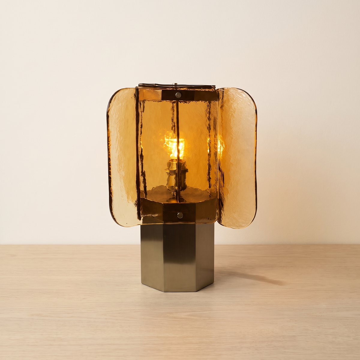 Sunvara Amber Glass Panel Table Lamp: table lamp with 4 curved amber textured glass panels arranged around a candle-style bulb, on a hexagonal brushed brass base