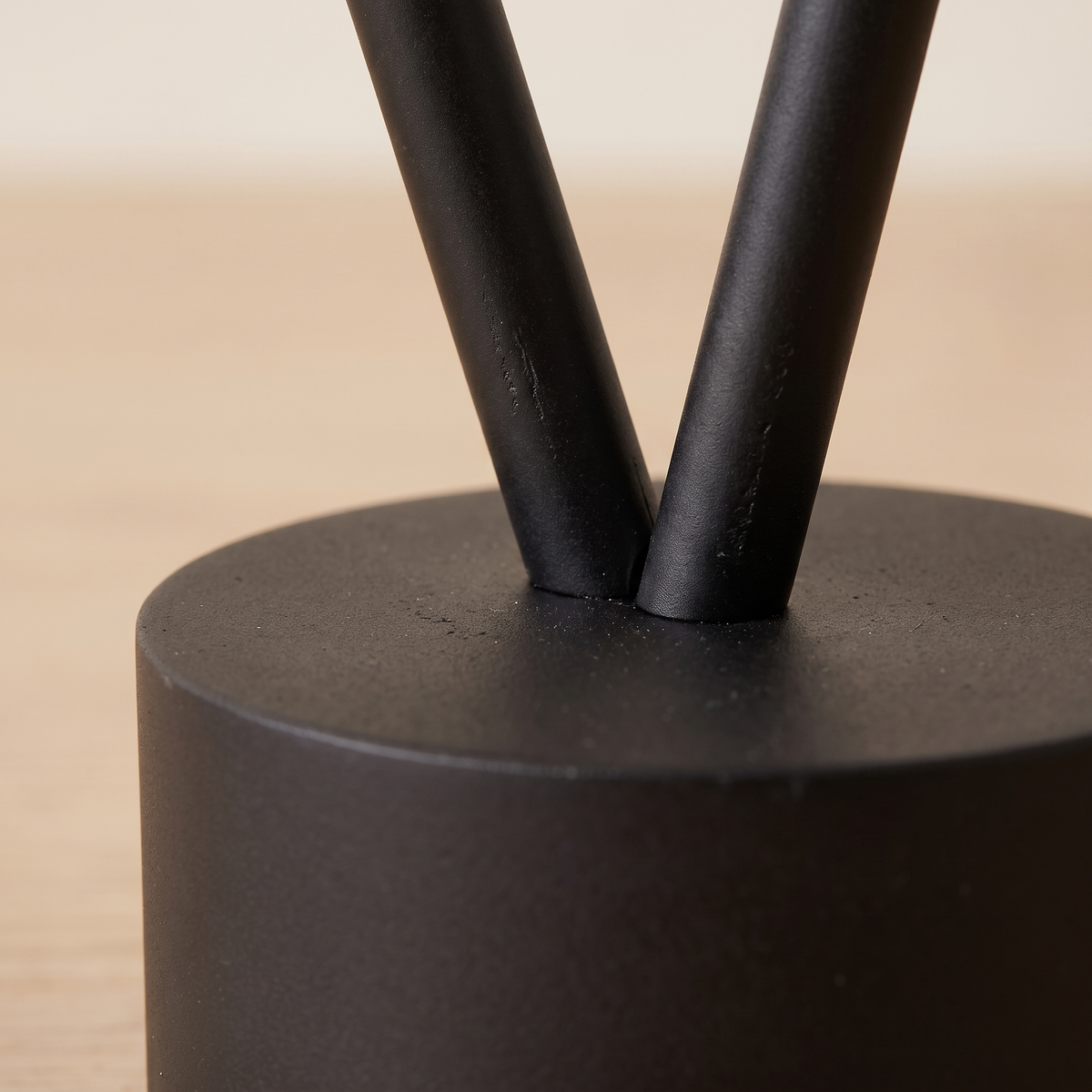 Tensara Elastic Strip Floor Lamp: minimalist floor lamp made of 1 thin straight matte black rod leaning diagonally, its lower end in a small black cylinder floor weight and its top end resting against the wall, close-up detail