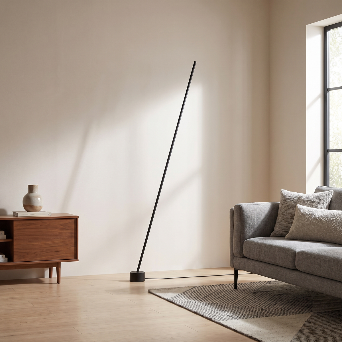 Tensara Elastic Strip Floor Lamp: minimalist floor lamp made of 1 thin straight matte black rod leaning diagonally, its lower end in a small black cylinder floor weight and its top end resting against the wall, shown in a room setting