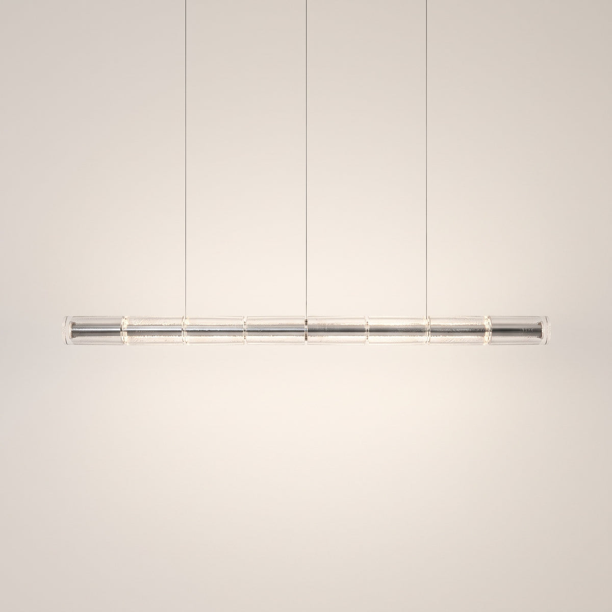 Cadressa Glass Chandelier, linear bar of eight textured clear glass sections with chrome core, lit, on a warm off-white studio backdrop