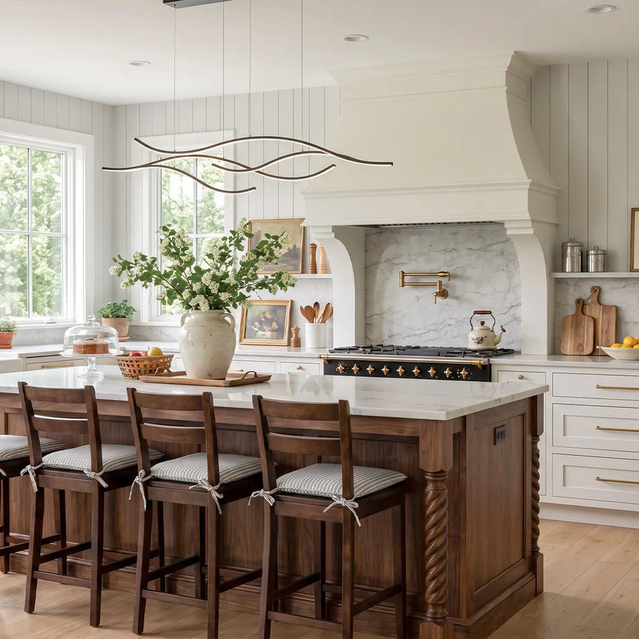 Linear pendant light made of wavy chrome-coloured LED bars hung from a slim rectangular canopy above a kitchen island with wooden stools.