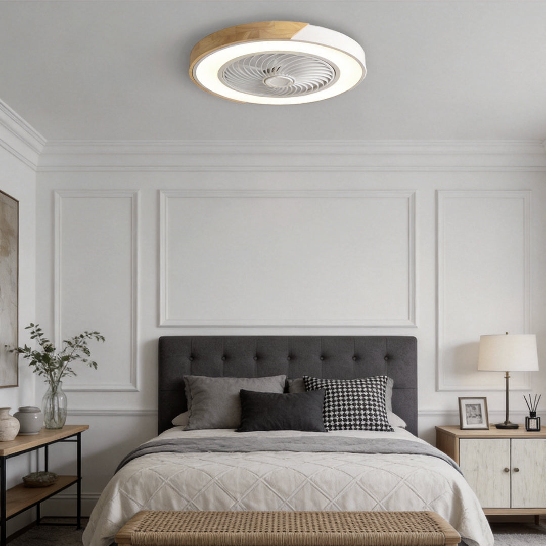 Round white and wood-grain bladeless ceiling fan with light, lit, on the ceiling of a white panelled bedroom.