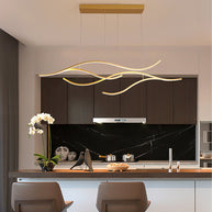 Linear pendant light made of wavy gold-coloured LED bars hung from a slim rectangular canopy above a kitchen island with a dark stone splashback.
