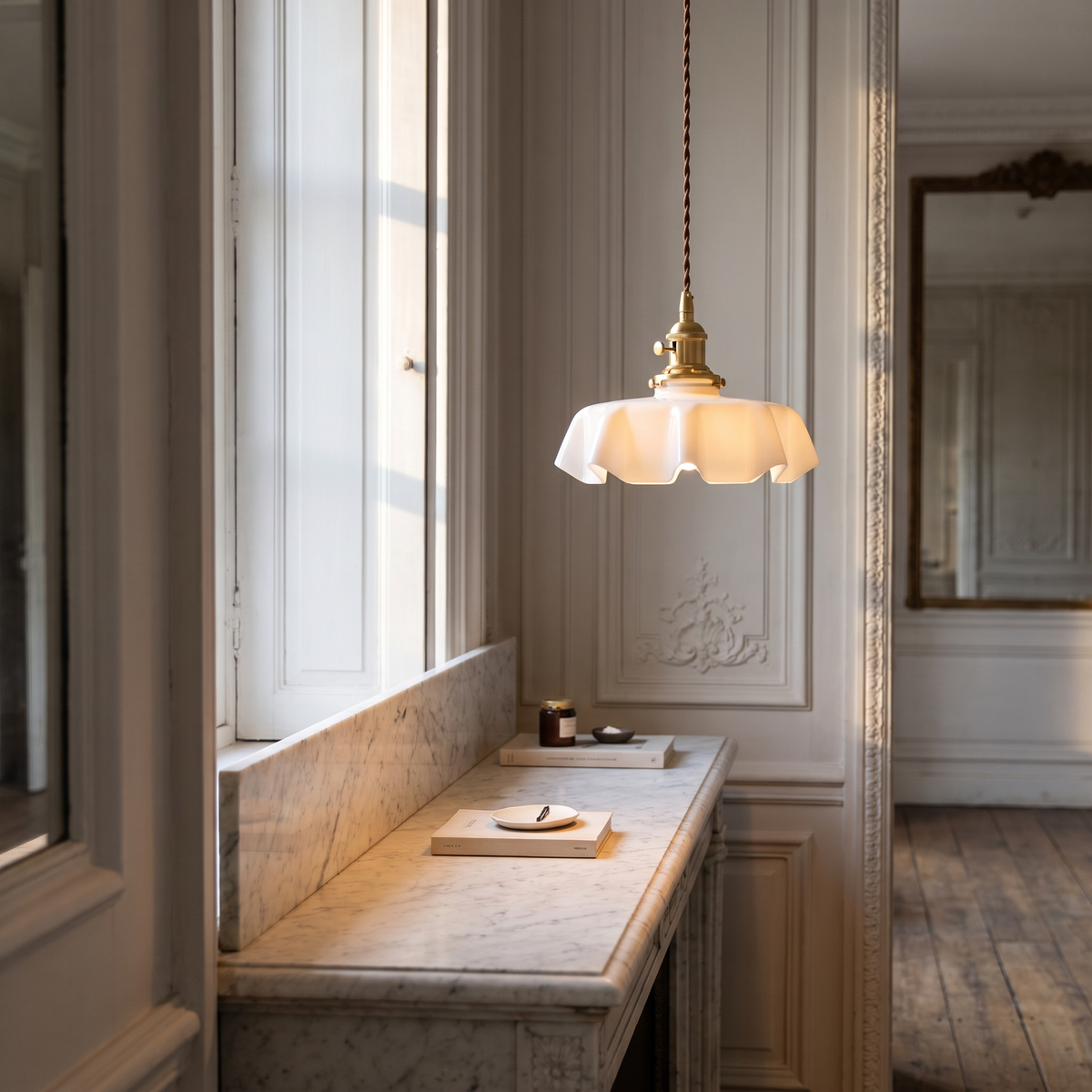 Fleurine pendant with a white scalloped glass shade on a brass body and brown twisted cable, hanging above a marble console in a panelled French-style hallway.