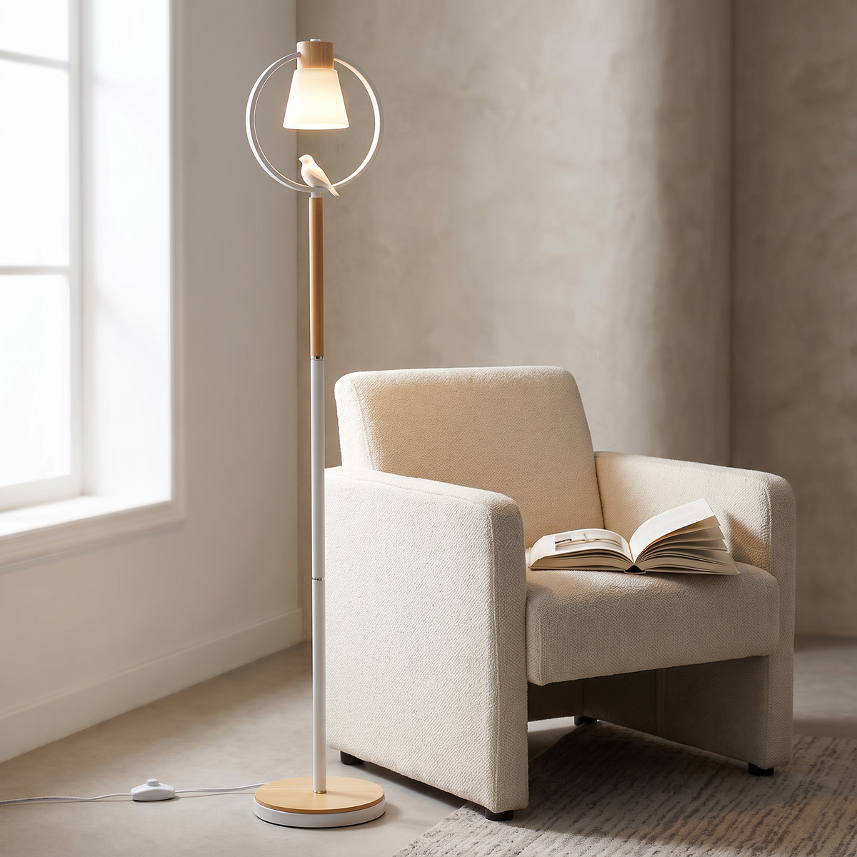 Belcaro floor lamp with a white cone shade inside a wood-topped ring and a small white bird on the ring, standing beside a cream armchair holding an open book.