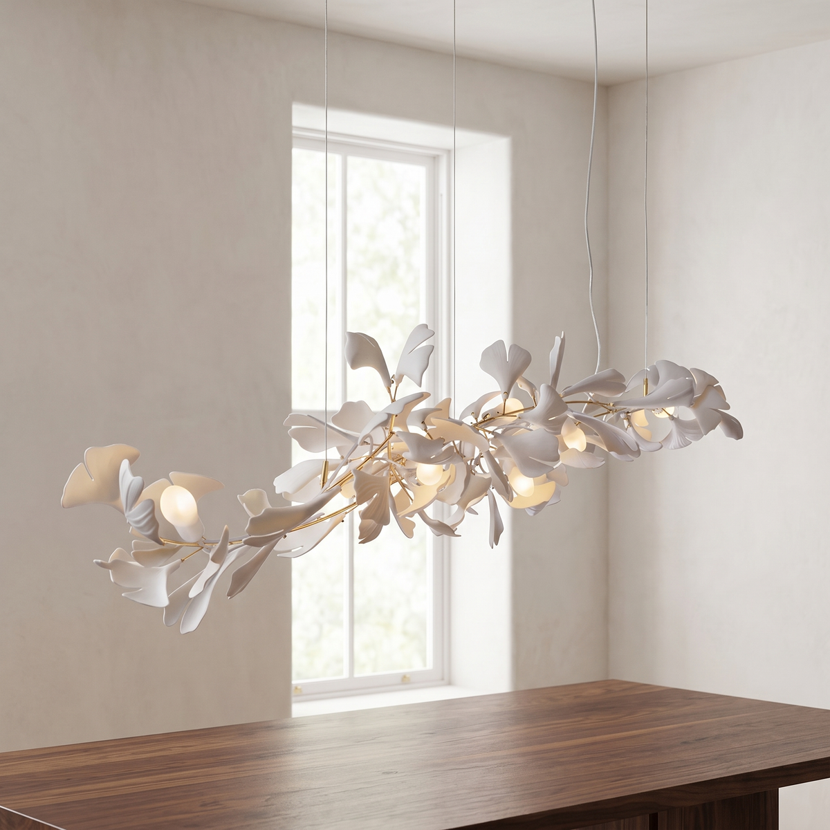 Zephrine linear chandelier with a gold branch and white porcelain ginkgo leaves, suspended on thin cables above a table.