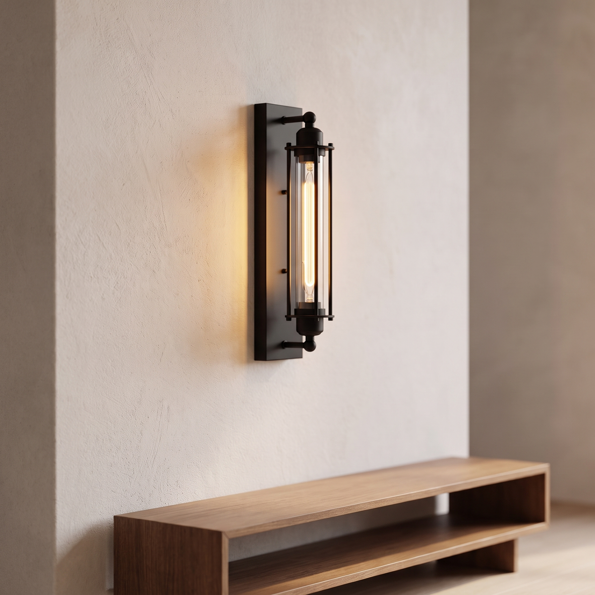 Corliss wall sconce with a black iron backplate and cage around a clear glass cylinder lit by a filament lamp, mounted alone on a pale plaster wall.