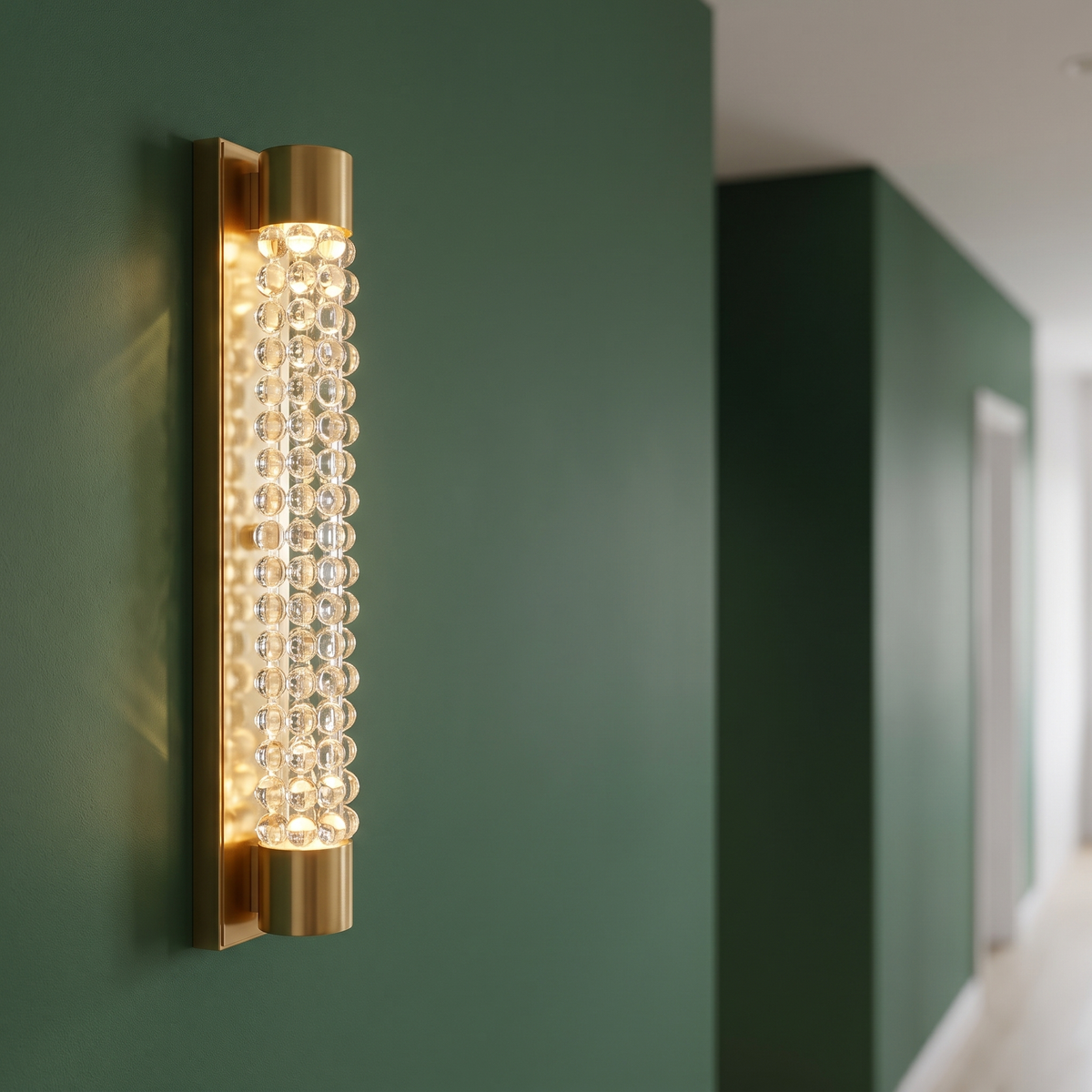 Quarine wall sconce, a slim gold bar enclosing a column of clear crystal spheres, mounted on a deep green hallway wall.