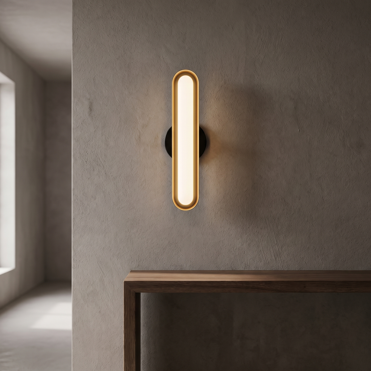 Zorelle wall light, a gold capsule with a frosted white lens, held off a plaster wall on a round black plate.