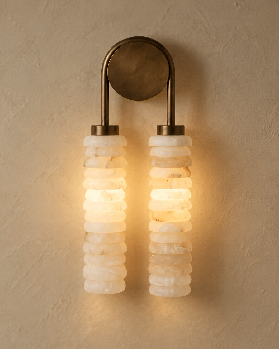 Calissa Ribbed Alabaster Sconce in antique brass, lit close-up of the two stacked alabaster columns glowing warm on a plaster wall